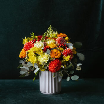 red yellow and red fresh flowers and foliage arranged in a white short ceramic vase