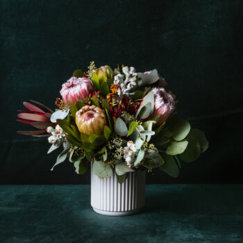 fresh native flowers and foliage arranged in a white short ceramic vase