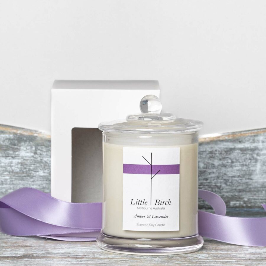 amber and lavender soy scented candle glass jar with lid display next to window face box and lavender ribbon for packaging