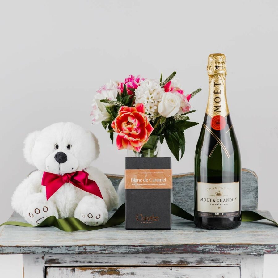 a gift pack including a bottle of French Moet Champagne a block of dark chocolate a teddy bear and a posy of seasonal flowers
