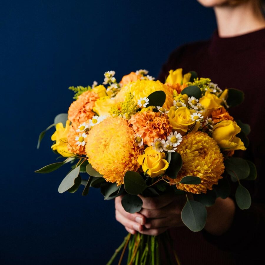posy made with vibrant orange and yellow flowers including roses disbud chrysanthemums golden rod marigolds and camomile flowers on a base of polygum eucalyptus