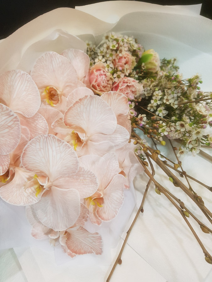 bouquet created with clustered mocha phalaenopsis orchids, peach frill tulips wax flower and spring budding branches