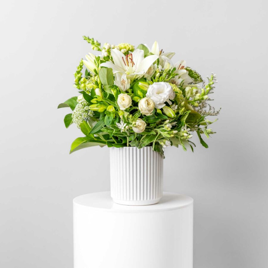short vase filled with fresh seasonal white flowers including lilies snapdragons roses alstromeria carnations tweedia lisianthus queen anne's lace and foliage