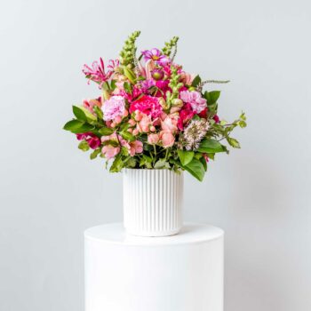short vase filled with fresh seasonal pink flowers including miniature roses snapdragons carnations cosmos lilies veronica nerines and alstromeria and foliage