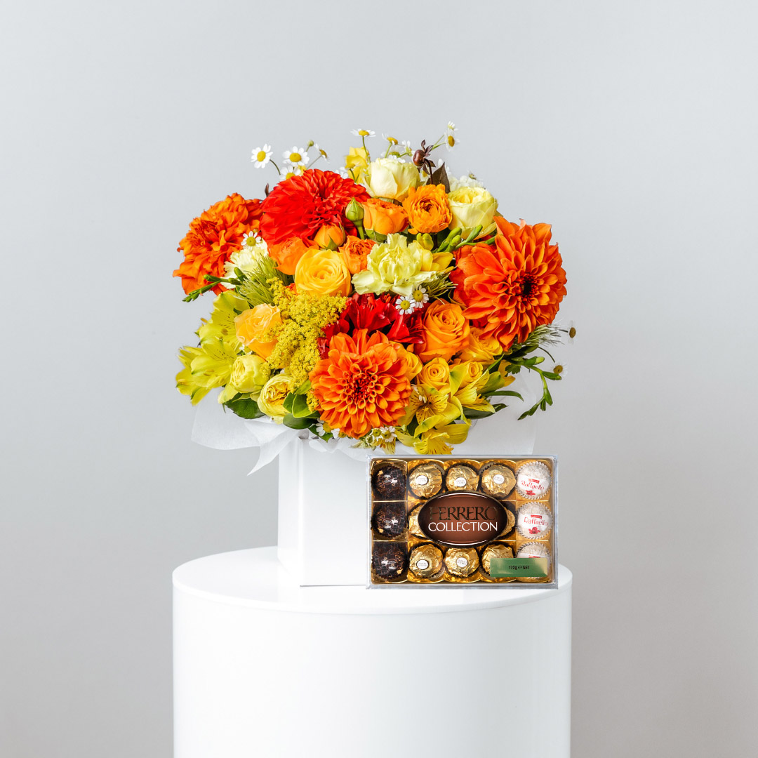 posy of fresh red yellow and orange flowers displayed in a white flower box behind a ferrero rocher chocolate box containing dark milk and white chocolates