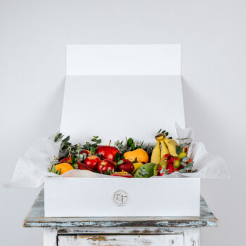 white sturdy box with lid filled with fresh fruit garnished with fresh foliage box is decorated with grosgrain ribbon