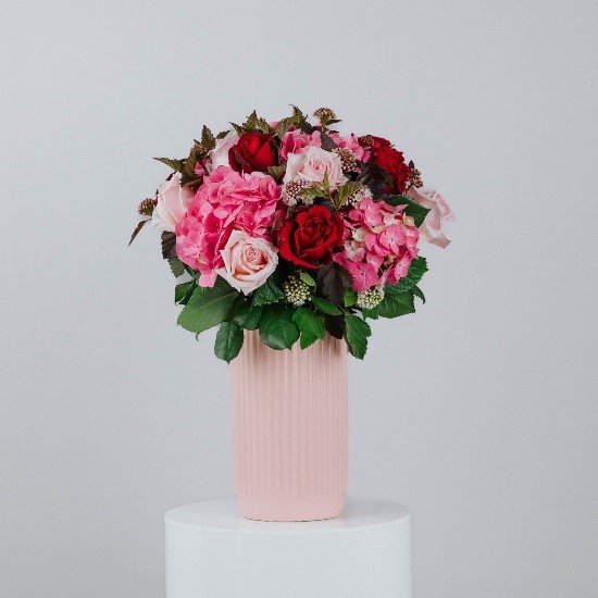 medium sized pale pink cylinder vase filled with red and pale pink roses including hydrangeas and foliage