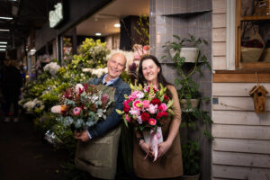 Joe and Hermina Bevilacqua holding fresh flower bouquets standing in front of their Camberwell Florist store